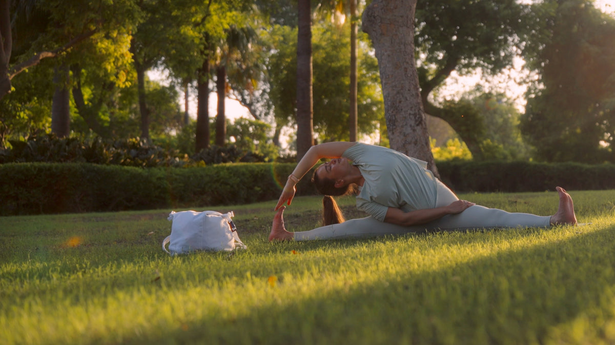Woman stretching on the grass in a sunlit park, wearing Bulleo
