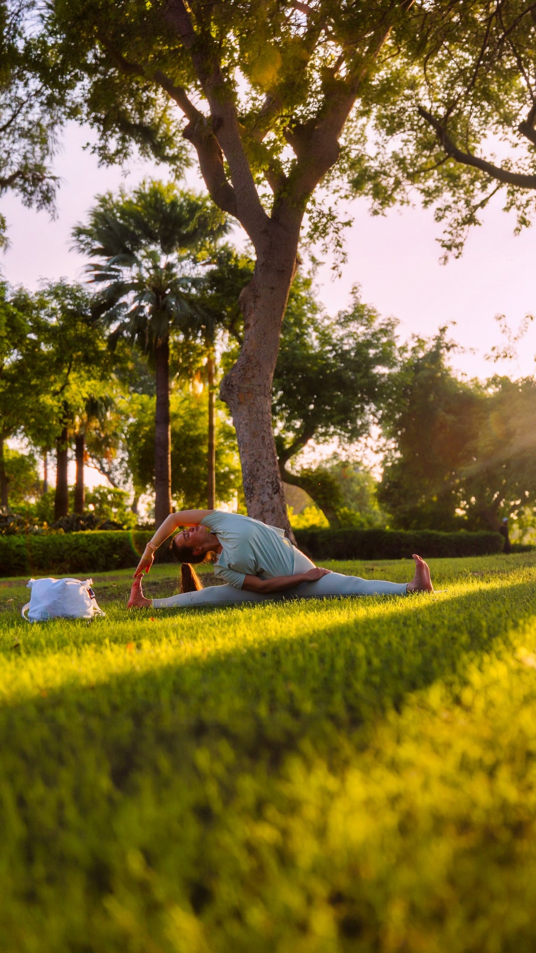Woman stretching on the grass in a sunlit park, wearing Bulleo